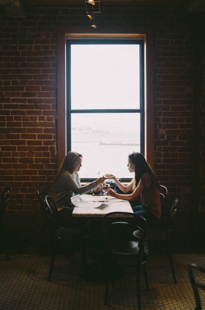 woman sitting in front of woman near window